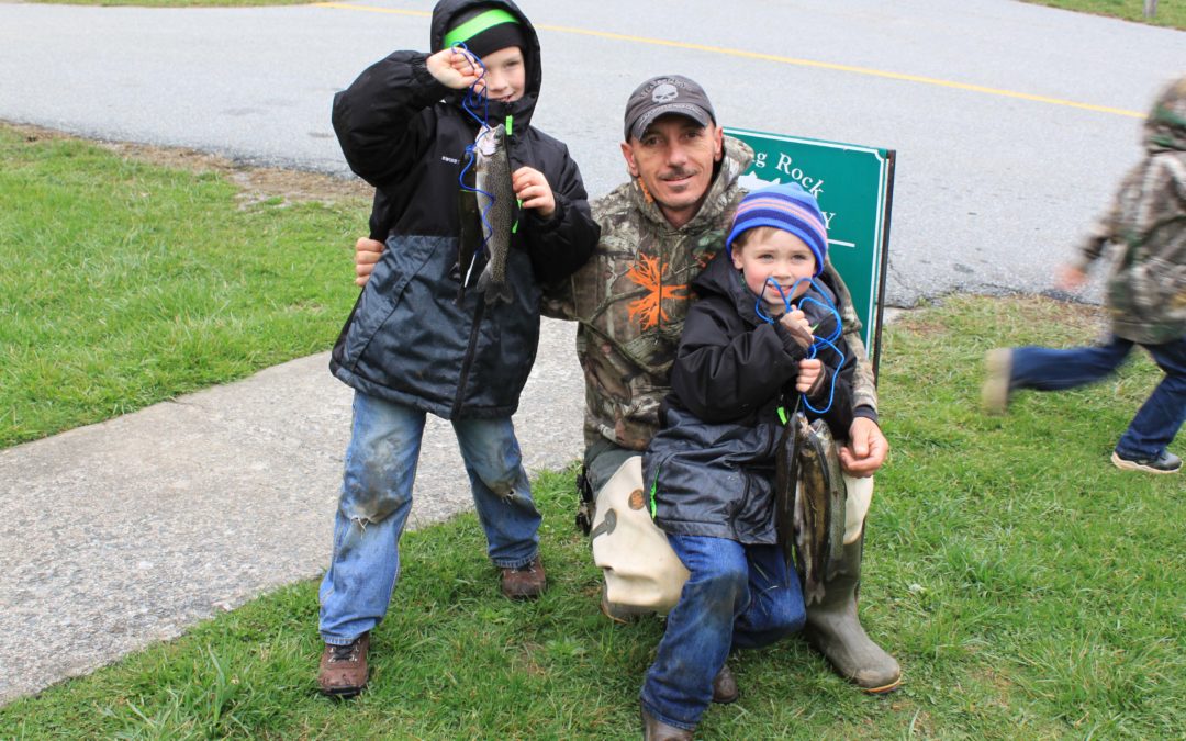 Two young boys excitedly pose alongside their grandfather with fish they caught at the Trout Derby