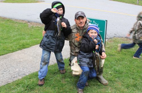 Two young boys excitedly pose alongside their grandfather with fish they caught at the Trout Derby