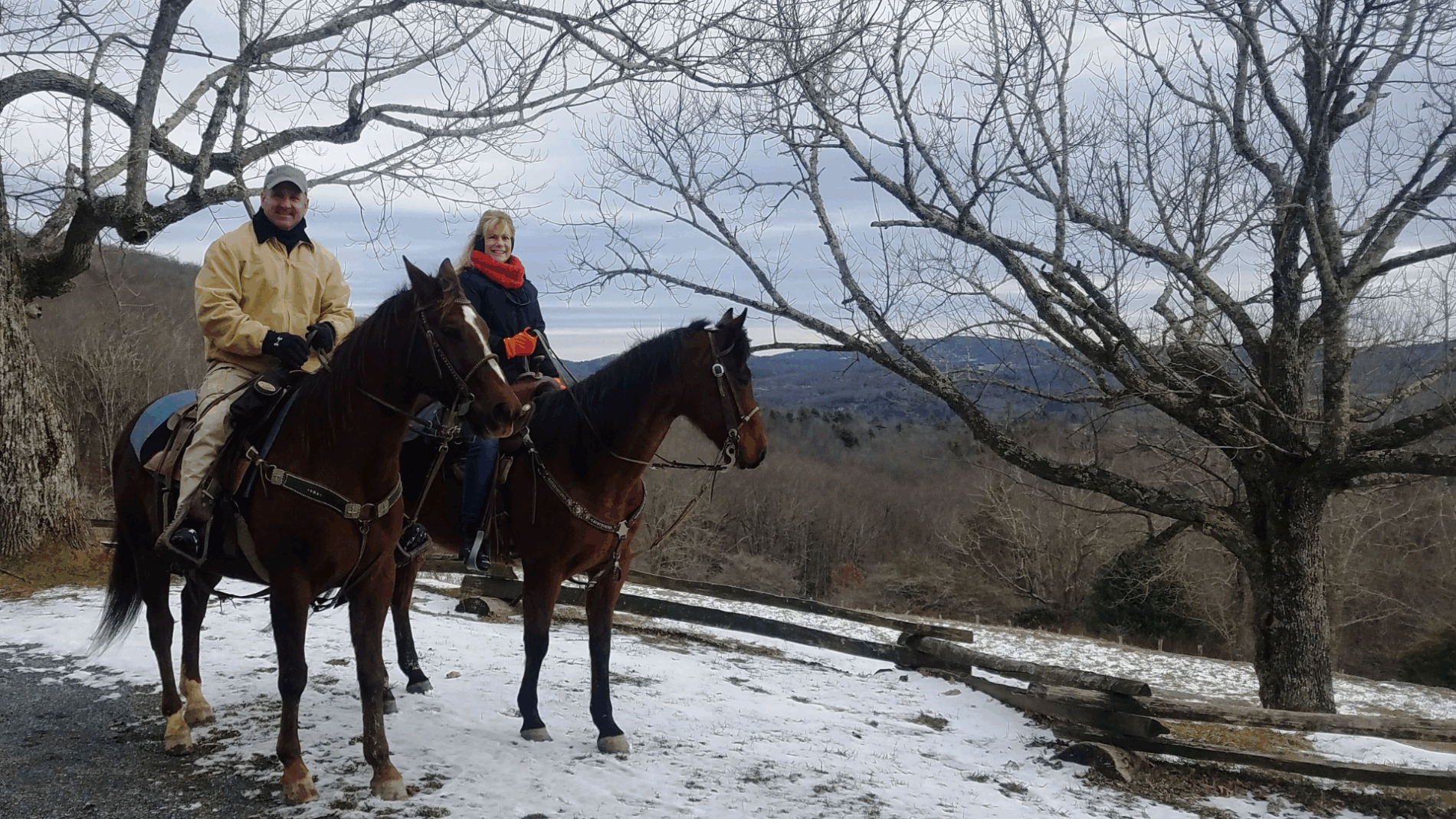 Two people sit on horses on a snowy day in front of the Blue Ridge Mountain winter landscape.