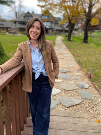 Young smiling woman in business casual clothing, standing outdoors.